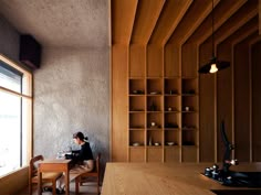 a woman sitting at a wooden table in front of a window next to a book shelf