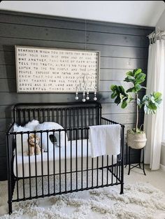 a baby's crib with white sheets and blankets on it, next to a potted plant