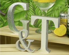 two silver letters sitting on top of a wooden table next to a bottle of alcohol