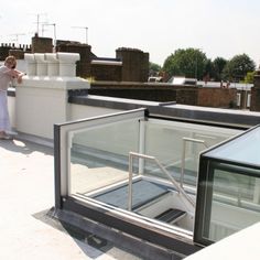 a woman standing on top of a roof next to a glass enclosure with an open door