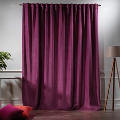 a living room with purple curtains and pink pillows on the floor next to a lamp