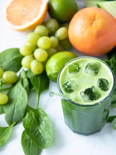 a green smoothie in a glass surrounded by fruit