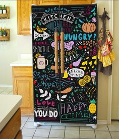 a black refrigerator covered in lots of doodles and writing on the front, next to a kitchen counter