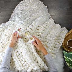 a woman is crocheting a blanket on the floor with her hands and fingers