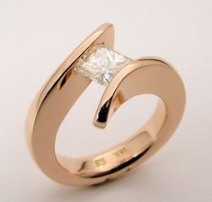 a gold ring with a princess cut diamond in the center, on a white background