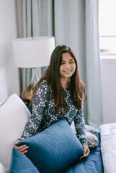 a woman sitting on top of a bed holding a blue pillow next to a lamp