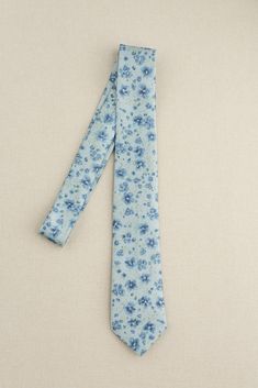 a tie with blue flowers on it is laying on the ground next to a white wall