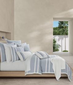 a bed with blue and white comforters in a room next to a window that has palm trees on it