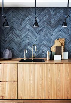 a kitchen with wooden cabinets and black wall tiles on the backsplash, along with brass faucets