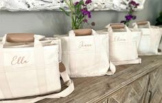 four personalized totes are lined up on a table with flowers in the background