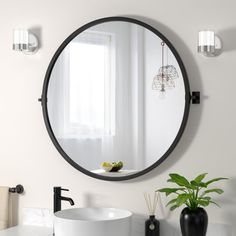 a round mirror hanging on the wall above a sink in a white bathroom with black fixtures