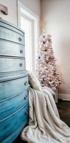 a blue dresser with a white christmas tree in the corner and a blanket on top