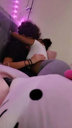 two people hugging each other while laying in bed with stuffed animals on the floor next to them