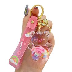 a hand holding a bear key chain with a pink case and rainbow charms on it