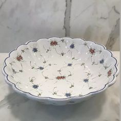 a white bowl with blue and red flowers on it sitting on a marble counter top