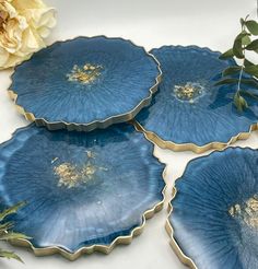 four blue plates sitting on top of a table next to a white flower and green leaves