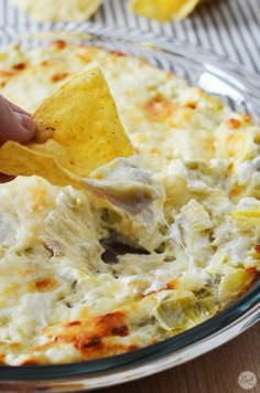 a person dipping a tortilla chip into a bowl full of dip and cheese