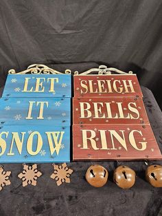 three wooden signs sitting on top of a black cloth covered table next to bells and snowflakes