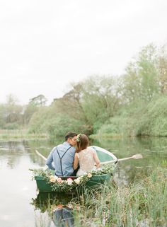 a man and woman sitting in a small boat on the water with greenery around them