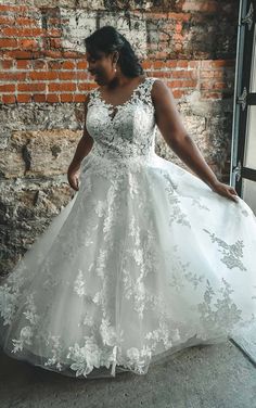 a woman in a white wedding dress is standing by a brick wall and posing for the camera