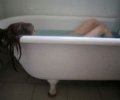 a woman laying down in a bathtub with her head on the back of the tub