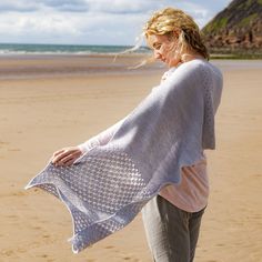 a woman standing on top of a sandy beach holding a white blanket over her shoulder