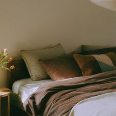 a bed that has some pillows on it and a vase with flowers in the corner