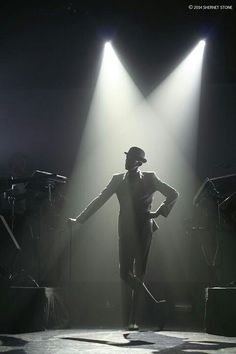 a man standing on top of a stage in front of three spotlights with his hands behind his back