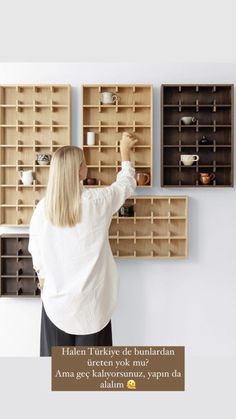 a woman is placing cups on the wall in front of shelves with coffee mugs