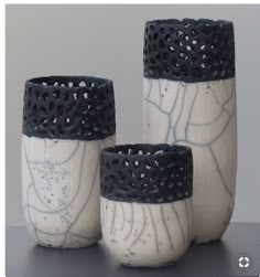 three white and black vases sitting next to each other on top of a table