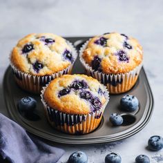 three blueberry muffins on a black plate with fresh blueberries around them