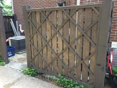 a wooden gate with lattice design in front of a brick building and trash cans on the sidewalk