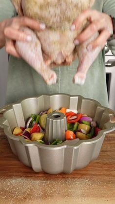 a person holding a chicken over a pan filled with vegetables