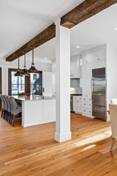 an open kitchen and dining room with white cabinets, wood flooring and exposed beams