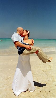 a bride and groom kissing on the beach with clear blue skies in the background at their wedding