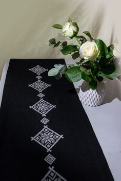 a black table runner with white roses in a vase