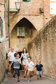 a group of people walking down a street next to a brick wall with an archway