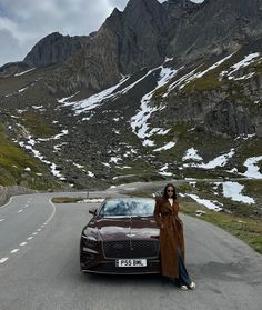 a woman standing next to a car on the road