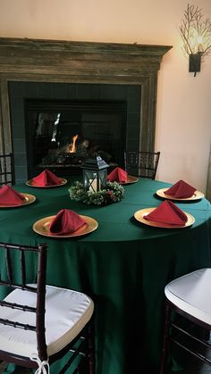 the table is set with red napkins and place settings in front of an open fireplace