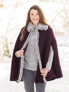 a woman standing in the snow wearing a purple and grey ponchle with sherph