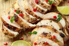 sliced chicken on a wooden cutting board with limes and peppers around the edges, ready to be served