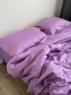 an unmade bed with purple sheets and pillows