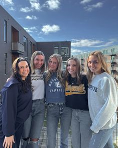 four girls are posing for the camera in front of some apartment buildings on a sunny day