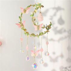 a dream catcher with pink flowers and crystals hanging from it's sides, in front of a white wall