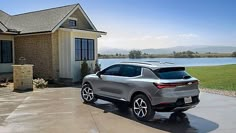 a silver suv parked in front of a house next to a body of water on a sunny day