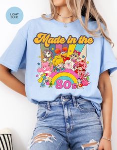 Step into a time machine of memories with our "Born in the 80s Nostalgia Retro Blast Tee." This vintage-inspired shirt is a vibrant tribute to the iconic era, featuring beloved characters like Strawberry Shortcake and her whimsical friends. Crafted from soft, comfortable fabric, this tee not only celebrates the spirit of the 80s but also offers a cozy fit for everyday wear. The lively design showcases a medley of colorful characters, bringing a burst of nostalgia to your wardrobe. Whether you're reliving your own 80s adventures or introducing the magic to a new generation, this tee is a perfect way to make a statement. Embrace the charm, fun, and enduring appeal of the 80s with every step you take in this delightful piece. Join us in celebrating the era that left an indelible mark on pop c Vintage Crew Neck T-shirt With Cartoon Print, Retro T-shirt With Screen Print For Fan Conventions, Retro Blue T-shirt With Cartoon Print, Retro Graphic Print T-shirt For Fan Conventions, Retro Character Print T-shirt For Fan Conventions, Retro Crew Neck T-shirt With Character Print, Retro Cotton T-shirt With Cartoon Print, Vintage Tops With Graphic Print For Retro-themed Events, Vintage Graphic T-shirt For Fan Conventions