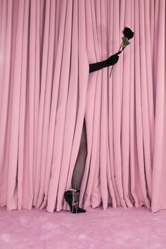 a woman standing in front of a pink curtain holding a rose up to her thigh