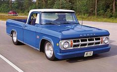 an old blue truck is driving down the road with another car in the back ground