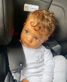 a little boy sitting in a car seat with his head turned to the side and looking at the camera