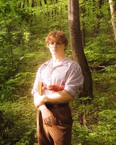 a man standing in the woods with his arms crossed and an apple in his hand